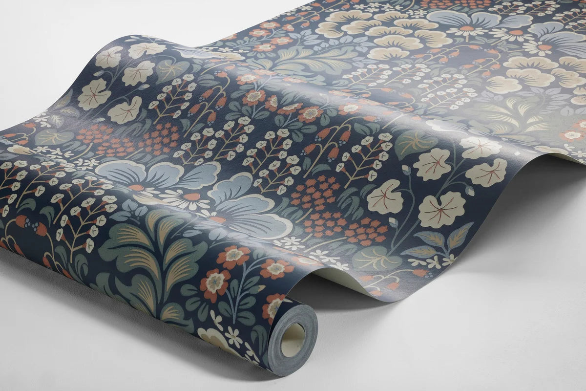 Set on a midnight blue background, our Blomstervall wallpaper in a surface print brings to life a lush pattern of green leaves, beige and blue puff-shapes, and red and white flowers.