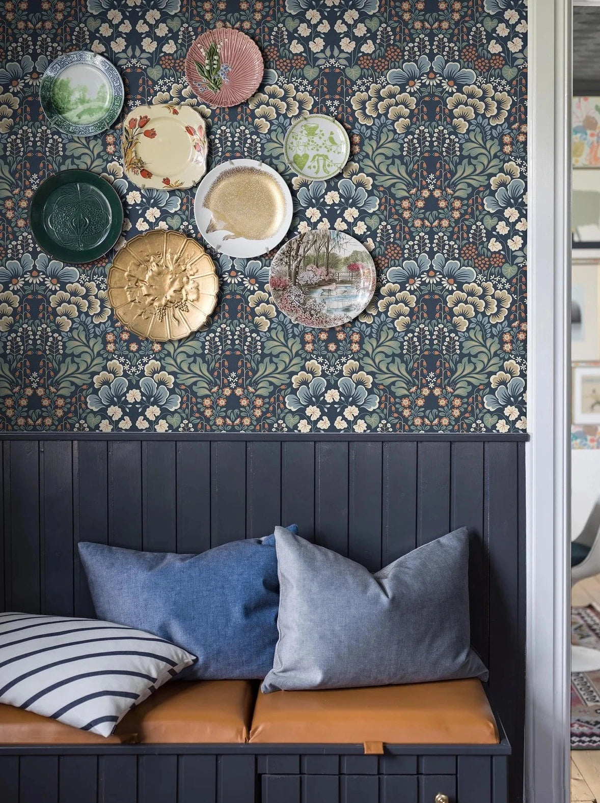 Set on a midnight blue background, our Blomstervall wallpaper in a surface print brings to life a lush pattern of green leaves, beige and blue puff-shapes, and red and white flowers.