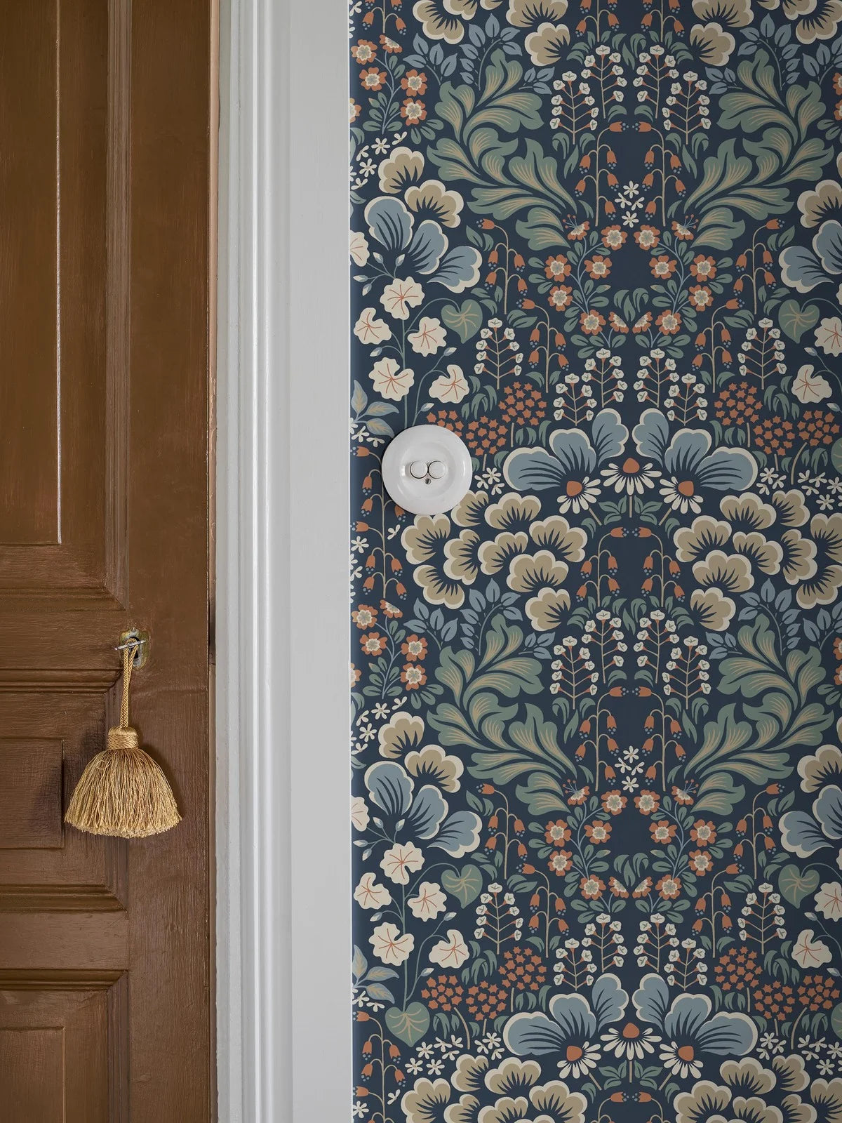Set on a midnight blue background, our Blomstervall wallpaper in a surface print brings to life a lush pattern of green leaves, beige and blue puff-shapes, and red and white flowers.