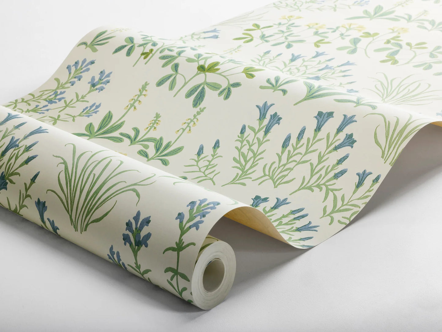 Echoing the lush and colorful spirit of a Swedish summer pasture, our Noras Äng wallpaper showcases a palette of green leaves and cheerful yellow and blue blossoms on a fresh white backdrop.