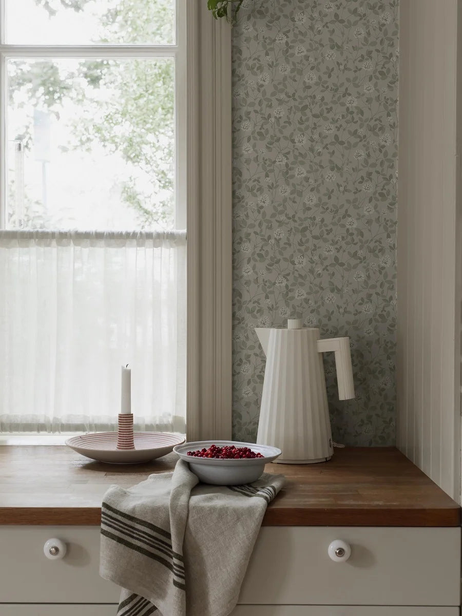 This beautiful Klöver wallpaper has warm white clover flowers among powdery olive-green leaves set on a light beige background.