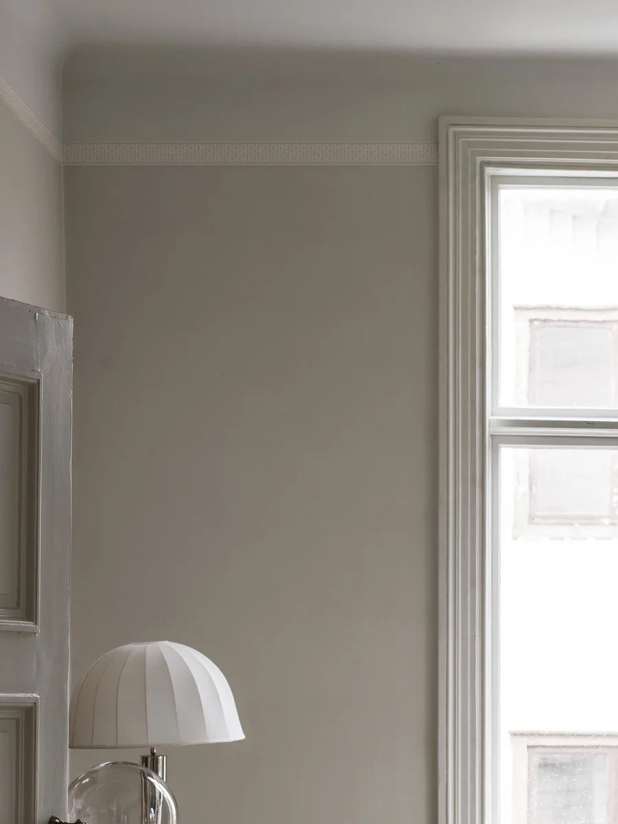 Featuring a dense yet subtle repeat geometric pattern, our Kalles Bård wallpaper border is colored in warm light beige tones and set on a fresh white background.