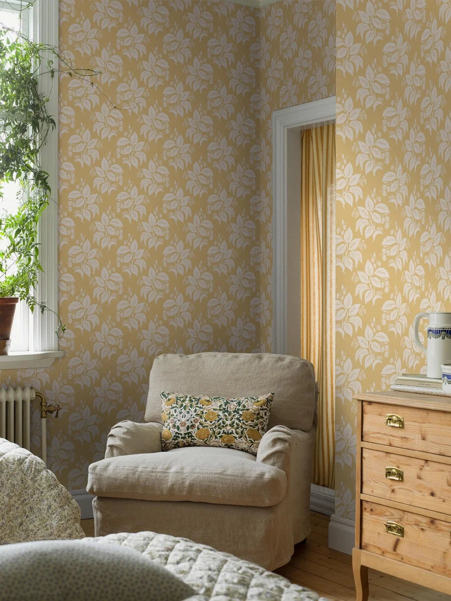 Our Tengbergska wallpaper offers a warm and cheerful take on an early 19th-century French wallpaper design, featuring a grey and white print on a yellow background.