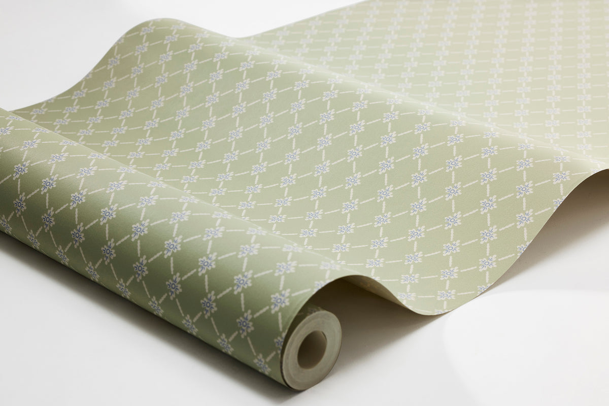 The lily-green Small-scale wallpaper Herman features a diagonal check pattern decorated with charming little flowers, here surface-printed in light beige and Dala blue.