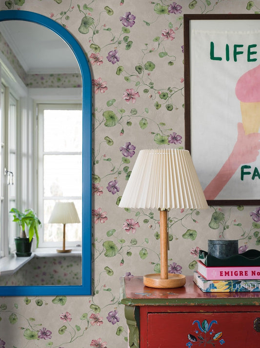 Violetta is a cozy, floral wallpaper, covered with delicate yet vibrant nasturtium flowers in pink and violet on a warm gray background, resembling a lime wall. 