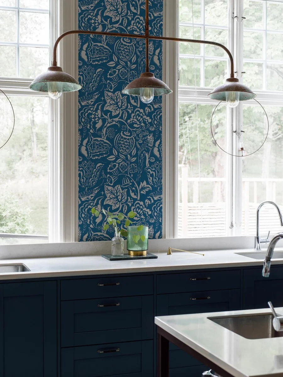 Wundervogel wallpaper in blue showcases whimsical birds and lush, winding plants in a large-scale pattern with modernist expressions evident in the pattern’s geometric and winding embellishments.