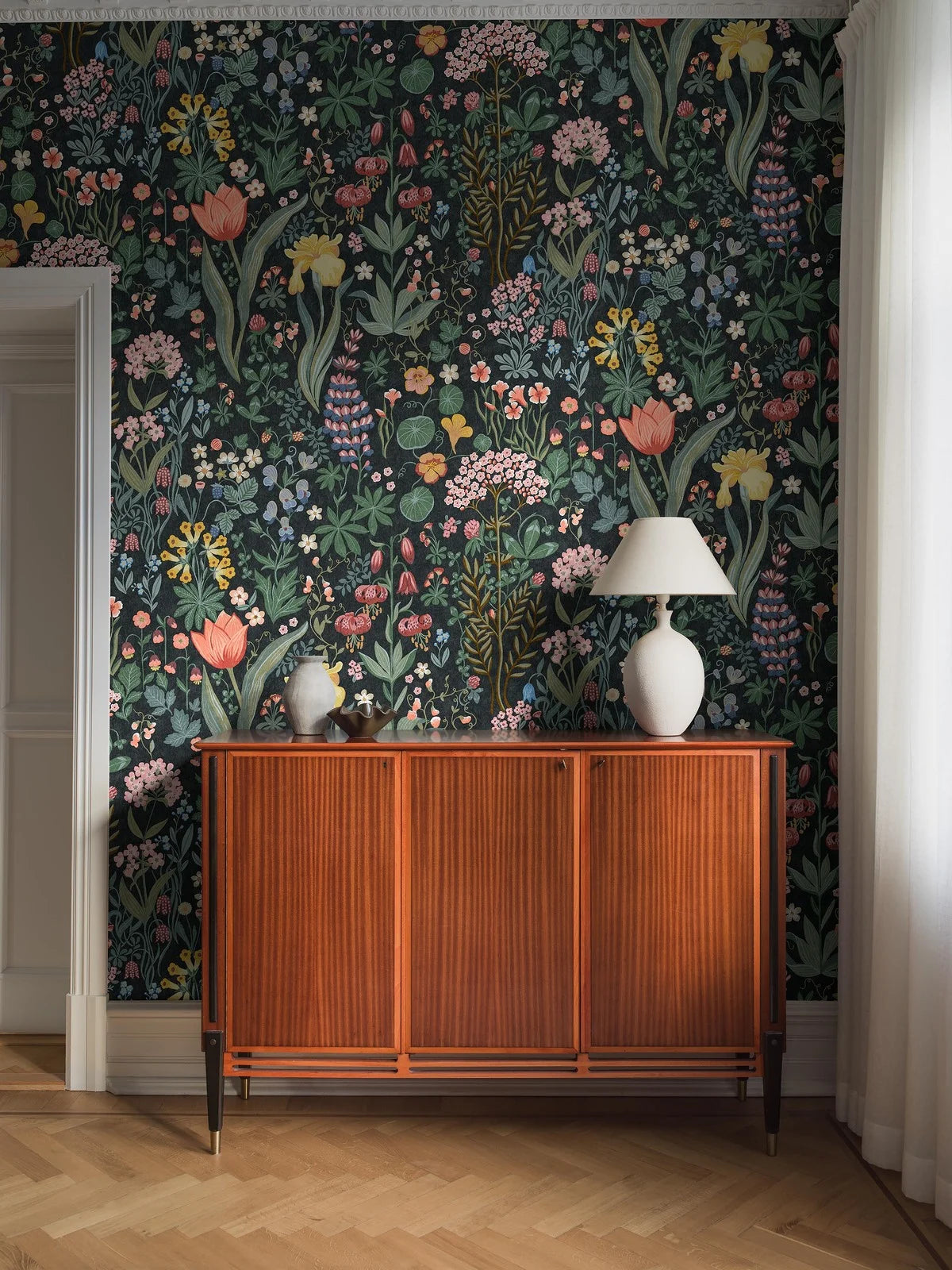 The Blomsterhav Grand wallpaper features a hand-painted, colorful floral pattern on a dark grey, almost black background.