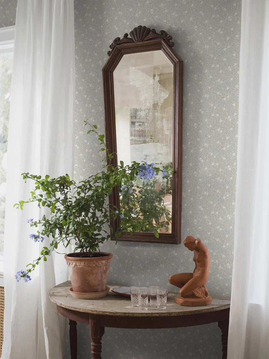 Step into a world of rustic charm with our Myrten wallpaper in a surface print. Colored in a palette of muted light blue, creamy white, and grey beige, it features a dense and decorative hand-painted floral and foliage pattern by Ulrica Hurtig.