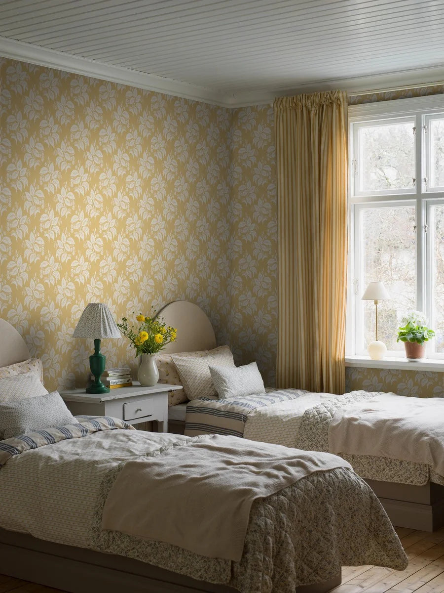 Our Tengbergska wallpaper offers a warm and cheerful take on an early 19th-century French wallpaper design, featuring a grey and white print on a yellow background.