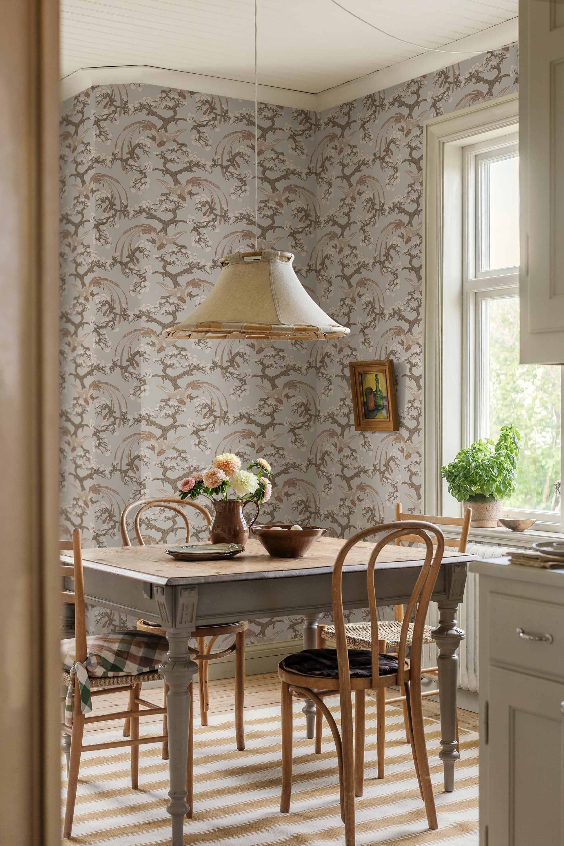 Fenix wallpaper pairs a warm brown-beige background with refined, hand-drawn birds resting among pine tree branches.