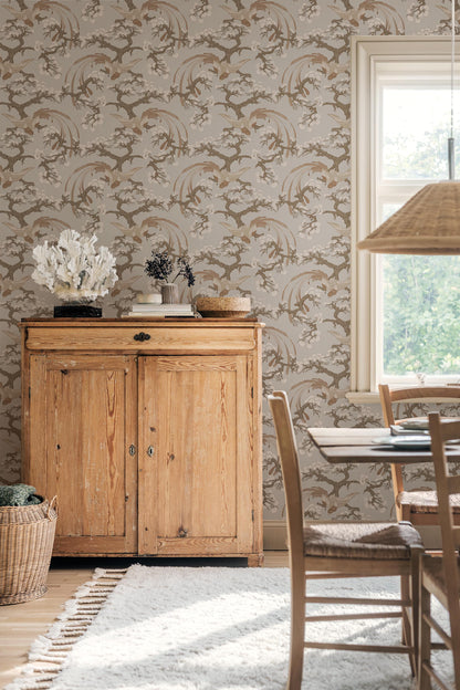 Fenix wallpaper pairs a warm brown-beige background with refined, hand-drawn birds resting among pine tree branches.