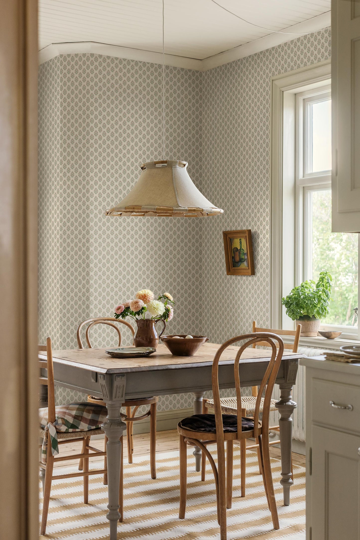 Set against a cream-white background, this Sibylla wallpaper is adorned with pale pink flowers with apricot centres and leaves in soft green tones, arranged in gentle, rhythmic bouquets.