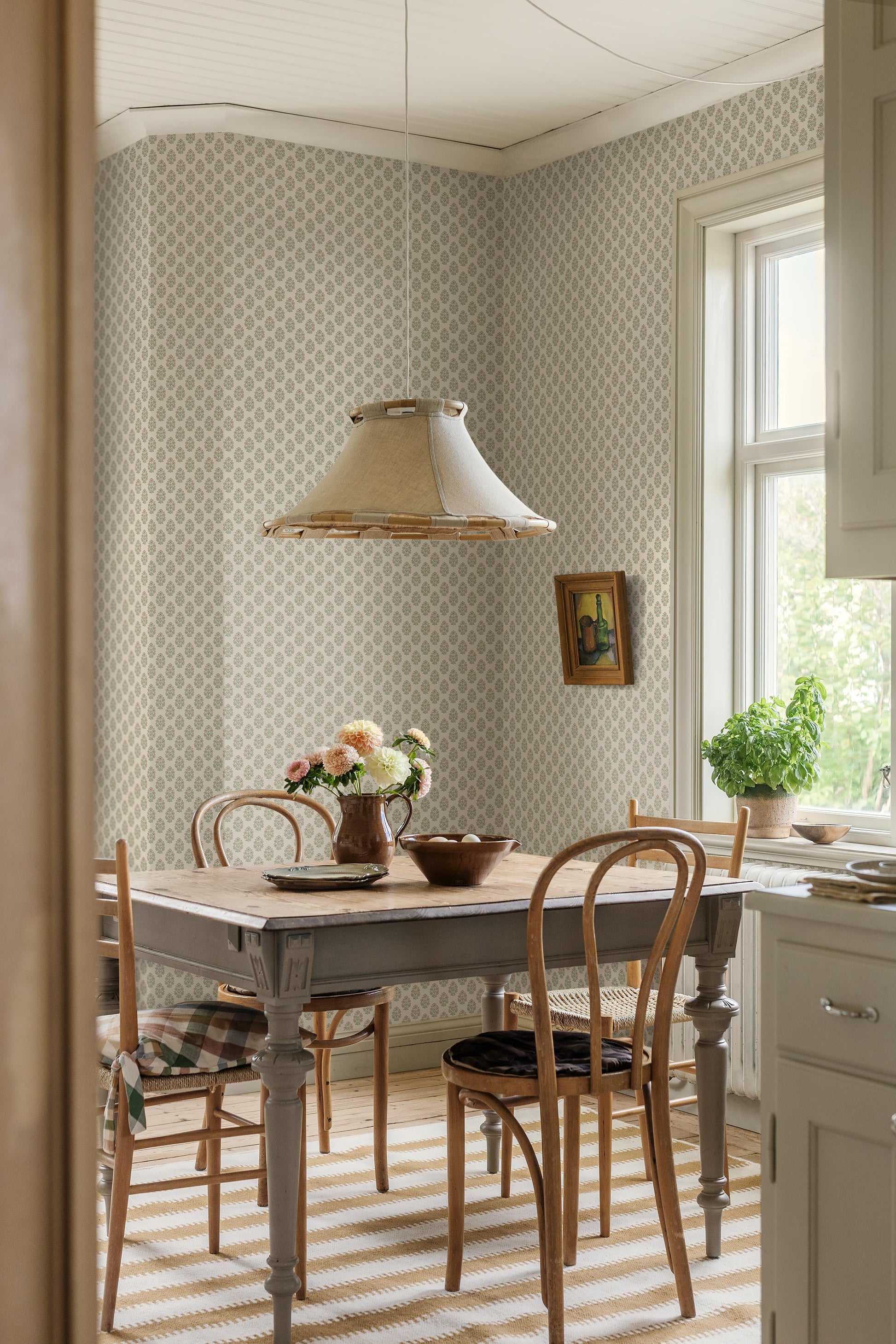 Set against a cream-white background, this Sibylla wallpaper is adorned with pale pink flowers with apricot centres and leaves in soft green tones, arranged in gentle, rhythmic bouquets.