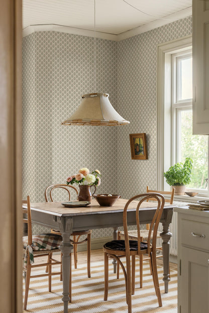 Set against a cream-white background, this Sibylla wallpaper is adorned with pale pink flowers with apricot centres and leaves in soft green tones, arranged in gentle, rhythmic bouquets.