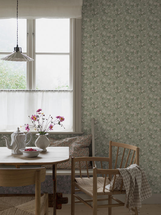Set on a light linden-green background, our Helena wallpaper displays blooming climbing roses alongside small white flowers in tones of beige, green, and white.