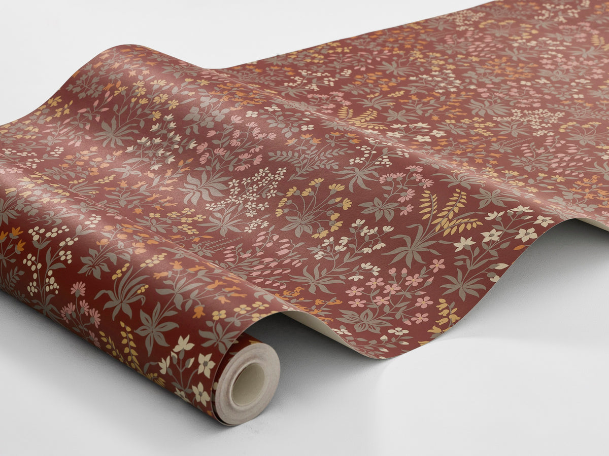 Sweet, stylised wildflowers in soft shades of grey-green, brick orange, warm white, yellow and Pink cover the red Vildflora wallpaper.