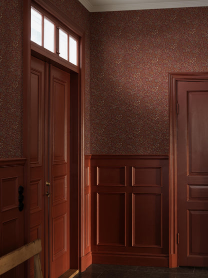 Sweet, stylised wildflowers in soft shades of grey-green, brick orange, warm white, yellow and Pink cover the red Vildflora wallpaper.