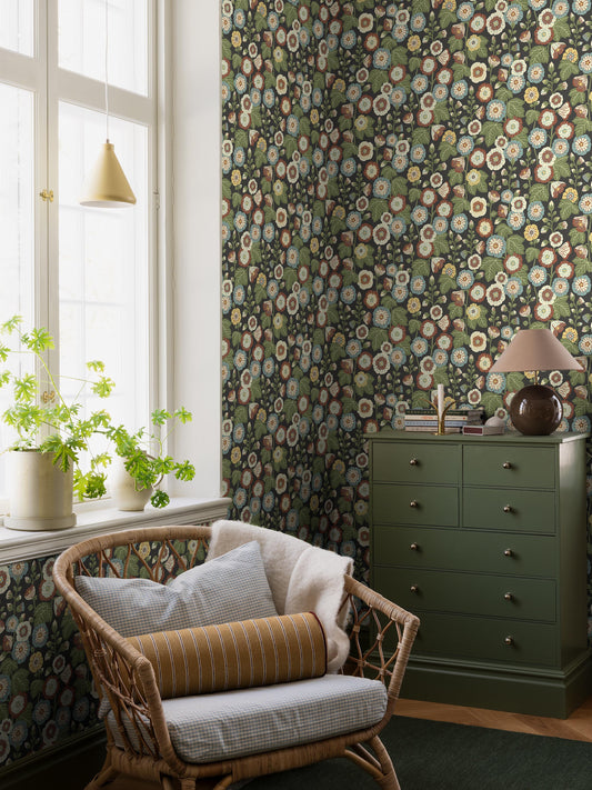 The black, Floral wallpaper Happy Hollyhocks is covered in hollyhocks, this magnificent plant that can stretch several metres up along fences and house walls and bears such magically beautiful flowers. A bold pattern, newly drawn in its entirety, yet in a cheerful, slightly naive retro style.