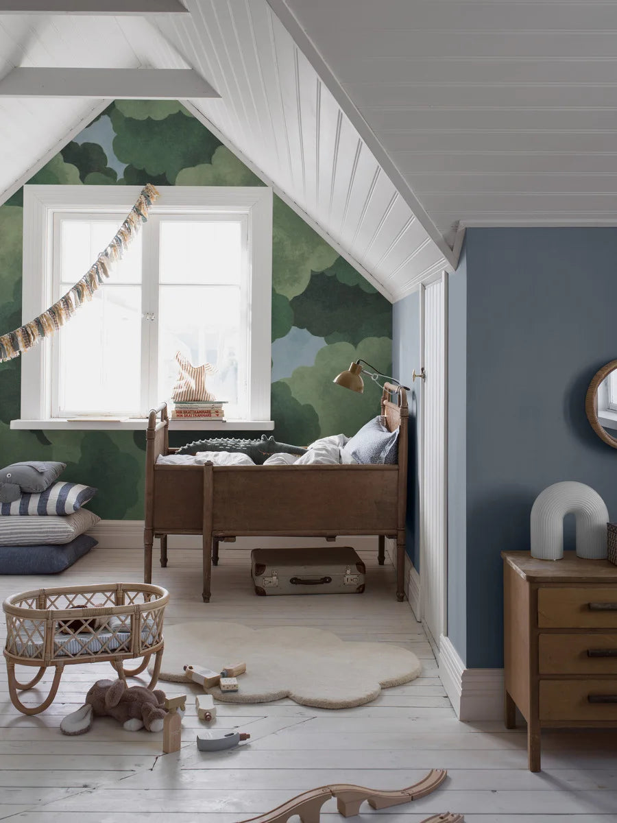 The children's wallpaper Under the Trees offers a new perspective – as if you're lying on your back, dreaming in the shade of rustling, green treetops with glimpses of clear blue sky.