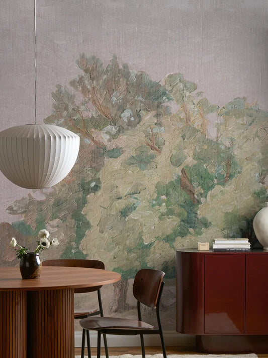 Like a large oil painting, the Hedgerow Landscape wallpaper stretches across the wall – an open landscape with softly shaped trees in hazy evening light.