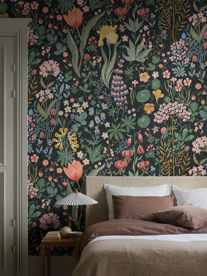 The Blomsterhav Grand wallpaper features a hand-painted, colorful floral pattern on a dark grey, almost black background. 