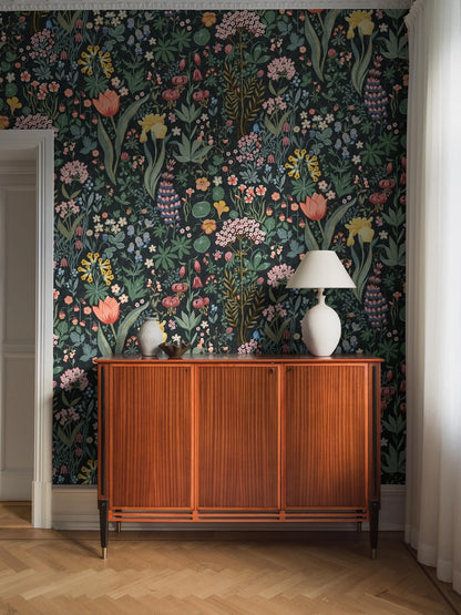 The Blomsterhav Grand wallpaper features a hand-painted, colorful floral pattern on a dark grey, almost black background. 