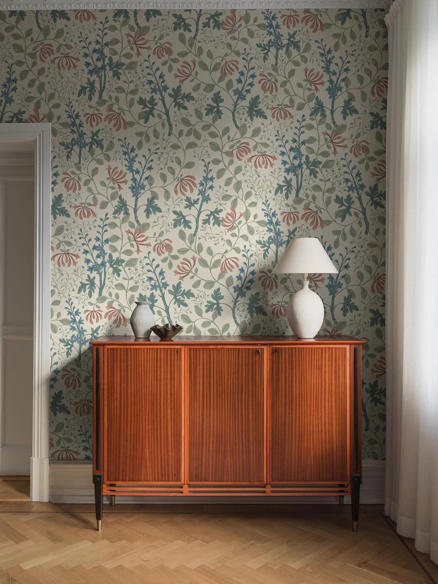 Across the light, large-floral Trädgårdsfröjd Grand wallpaper climbs a winding green foliage accented with blue delphiniums and pink honeysuckle on a cream-white background.