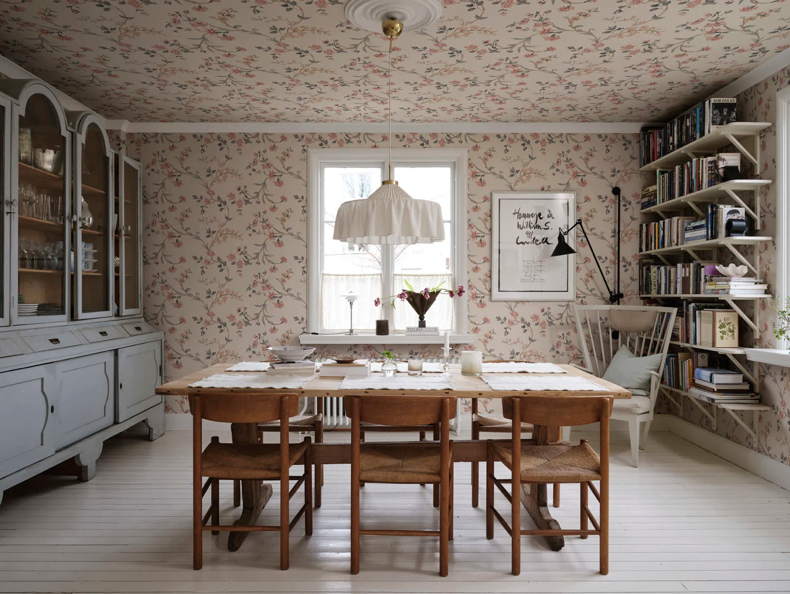 Soft wallpaper in its appearance and with a vintage feel. Clara, Pastel, has flowers in pale pastel blues, pinks, and blue on a beige background.