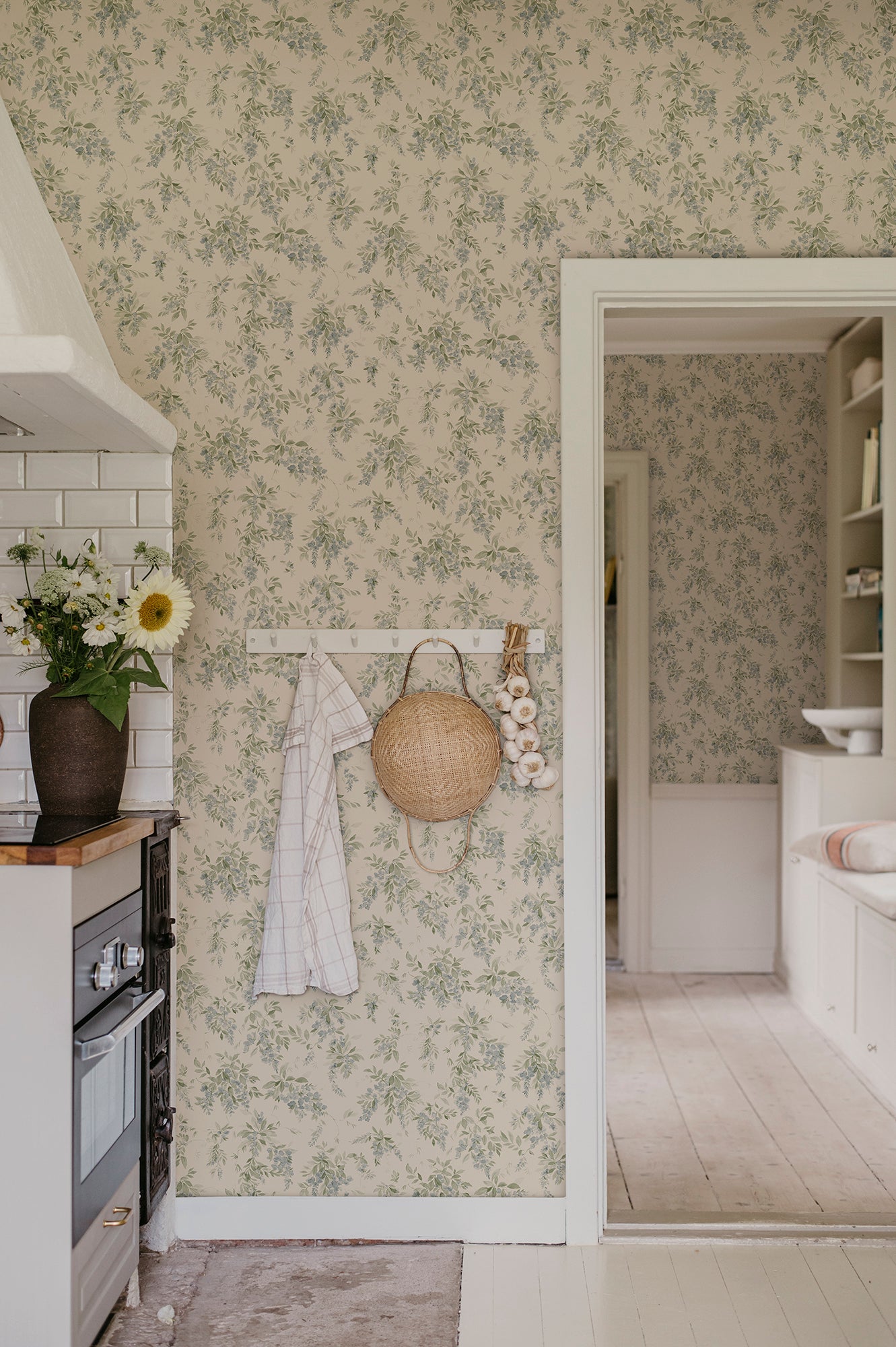 Wallpaper Lovisa with an airy watercolor featuring clusters of wisteria that exudes a romantic, rural charm with a contemporary touch. Lovisa, Blue, has a warm beige base with a delicate pattern in lovely soft blue and green hues.
