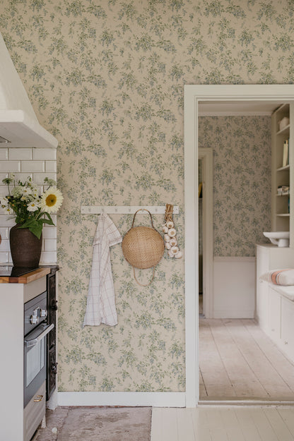 Wallpaper Lovisa with an airy watercolor featuring clusters of wisteria that exudes a romantic, rural charm with a contemporary touch. Lovisa, Blue, has a warm beige base with a delicate pattern in lovely soft blue and green hues.
