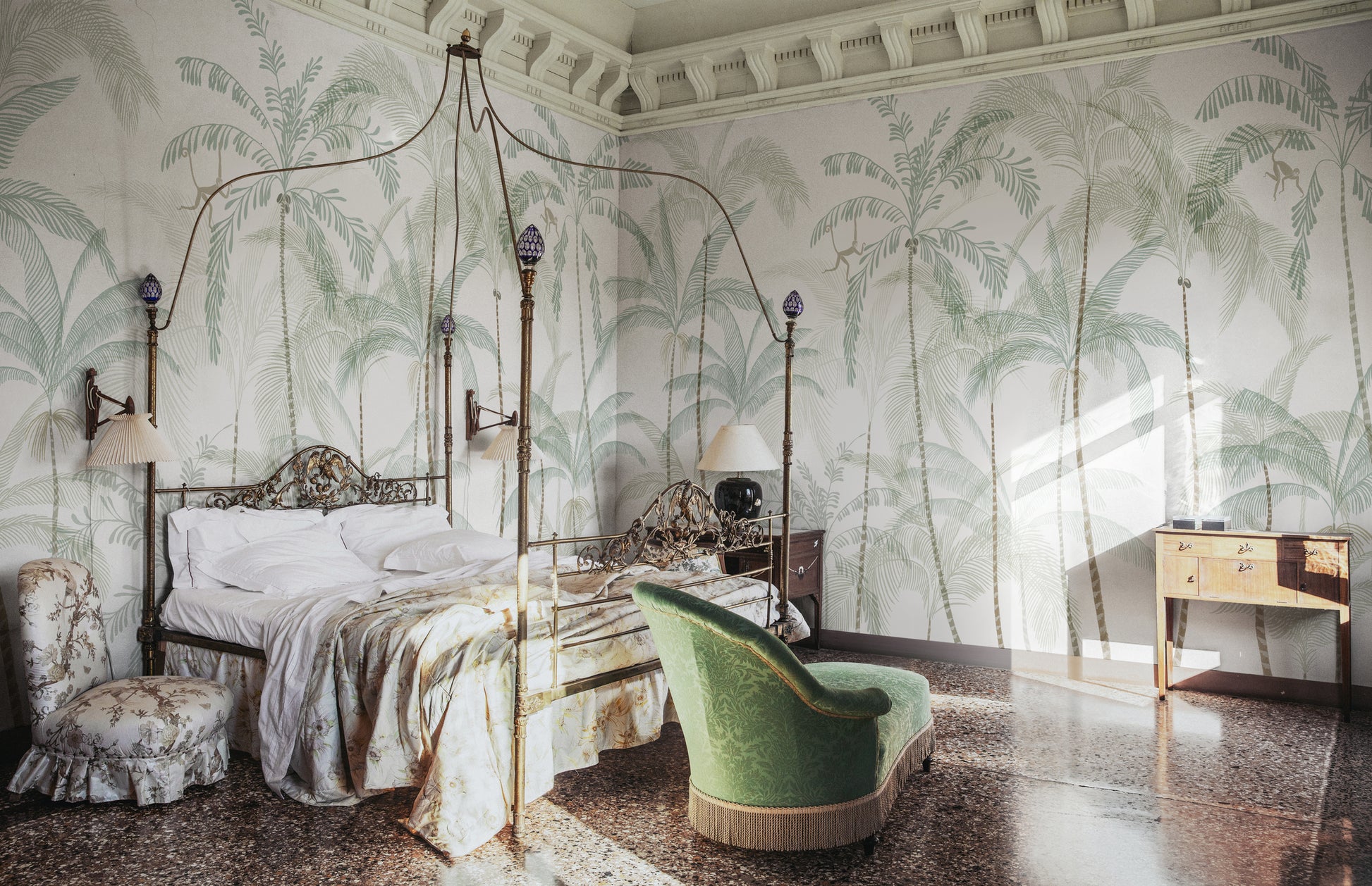 Hand-painted swaying palm trees with a vintage feel create a lush, airy scenography with monkeys swinging between the treetops. Wallpaper Louie, Light Green features a serene white background accented with delicate light green and soft beige hues.