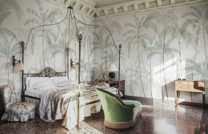 Hand-painted swaying palm trees with a vintage feel create a lush, airy scenography with monkeys swinging between the treetops. Wallpaper Louie, Light Green features a serene white background accented with delicate light green and soft beige hues.