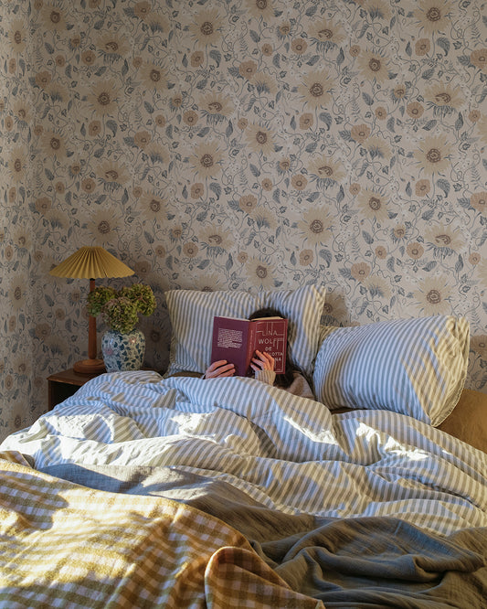 Wallpaper Solveig, Misty Blue, has a warm beige base adorned by flowers in warm beige and white, with misty blue foliage.